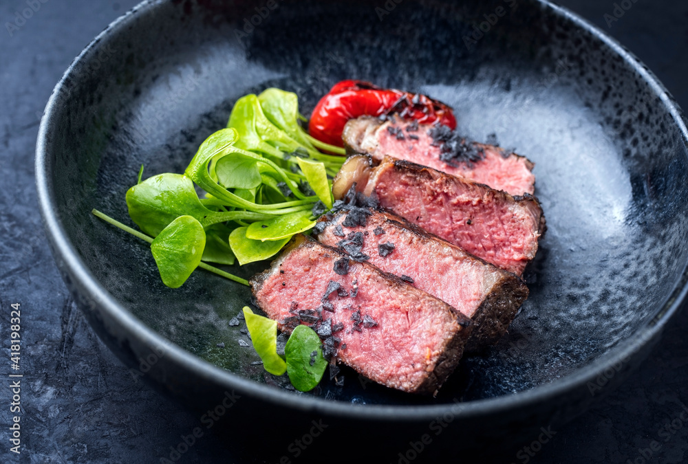 Modern style traditional dry aged sliced wagyu roast beef with fried onion rings served as close-up on a rustic black board Modern style traditional dry aged sliced wagyu roast beef with fried onion rings served as close-up on a rustic black board