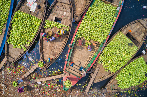 Aerial view of several small commercial boats with people unloading watermelons at Old Dhaka river port along Buriganga river in Dhaka, Bangladesh.
