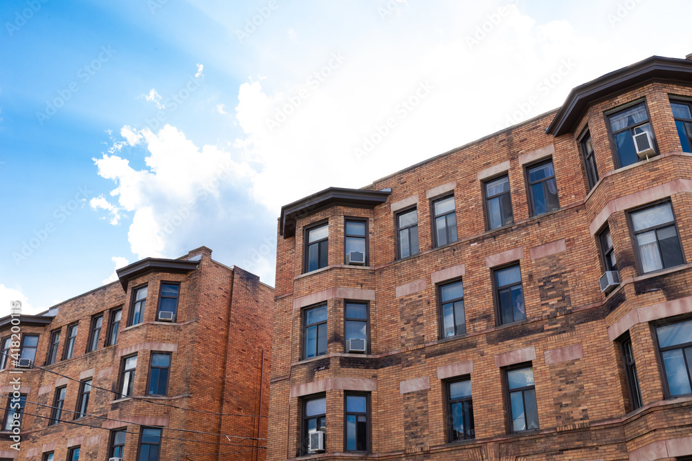 Old brick apartment buildings against bright blue sky with clouds, horizontal aspect