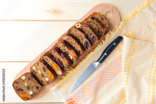 Freshly baked homemade bread with dried fruits, cut on a board and a knife on a wooden surface, top view.