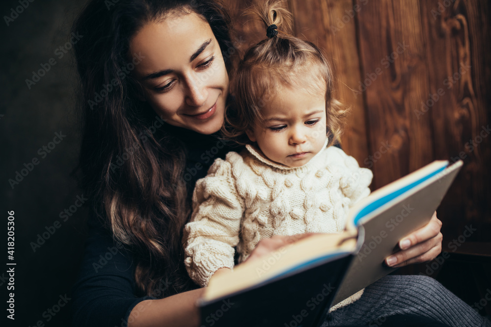 Young mother and her little daughter reading book together sitting in a comfortable chair. Young mother and her little daughter reading book together sitting in a comfortable chair.