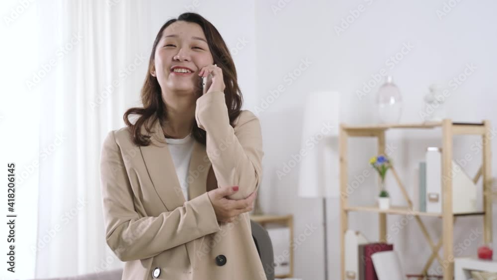 having delightful phone conversation at work. japanese woman manager holding her elbow and laughing happily talking to her friend during break. having delightful phone conversation at work. japanese woman manager holding her elbow and laughing happily talking to her friend during break.