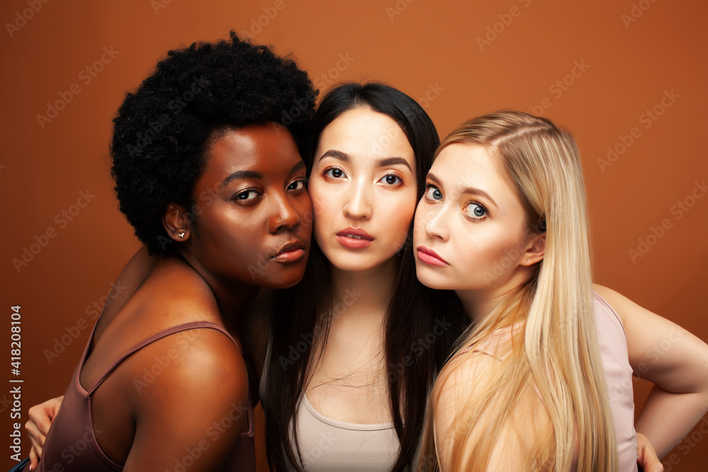 Obraz premium young pretty asian, caucasian, afro woman posing cheerful together on brown background, lifestyle diverse nationality people concept