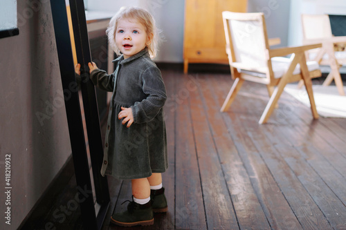 A surprised face. A small child girl is sitting at home looking in the mirror. Happy childhood, playing games at home. Modern interior in the apartment.