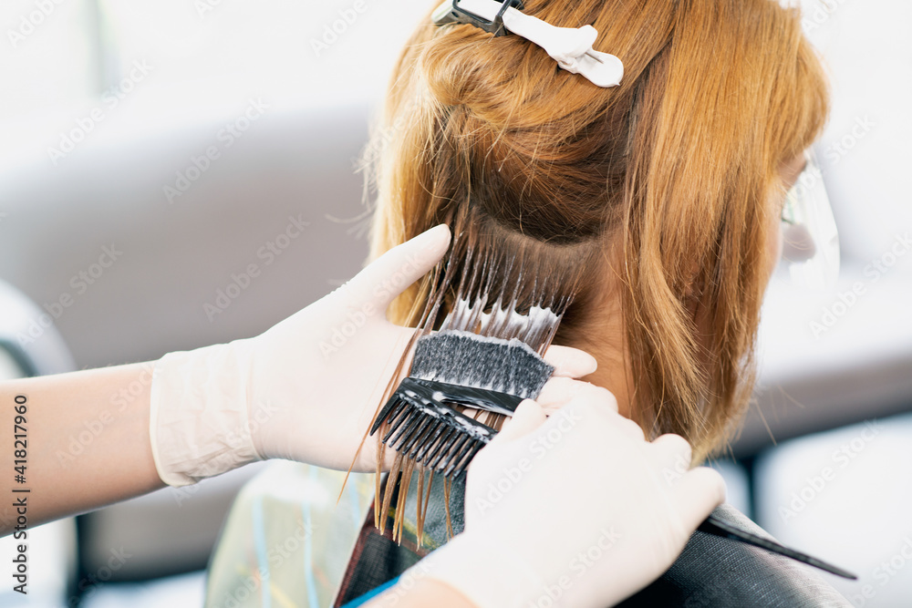 Fototapeta premium Back view of a female hairdresser doing a hairstyle for a redhead in a beauty salon. The process of styling hair in the hair salon..