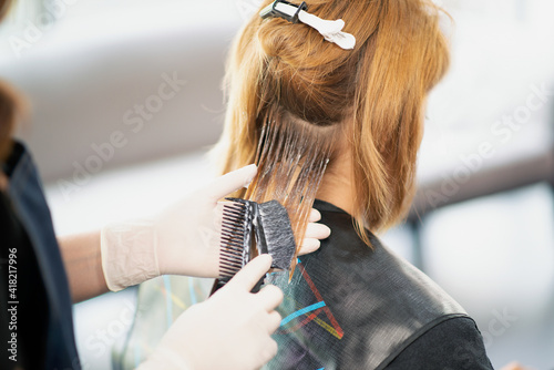Back view of a female hairdresser doing a hairstyle for a redhead in a beauty salon. The process of styling hair in the hair salon..