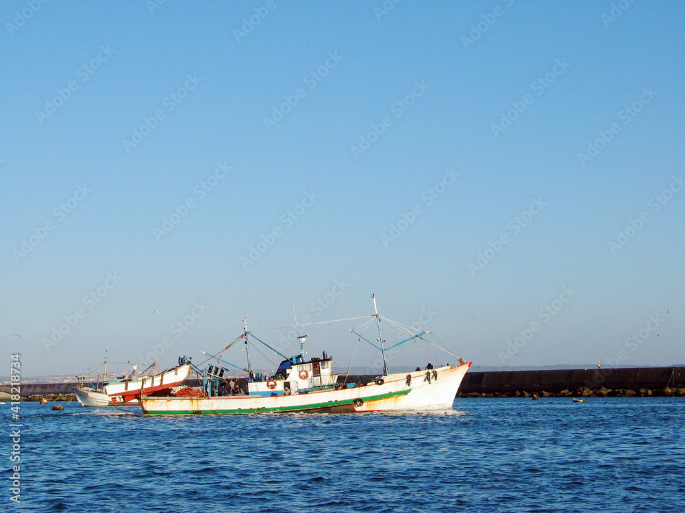 Commercial fishing boat in Portugal, inside harbor with visible seawall and calm blue water.