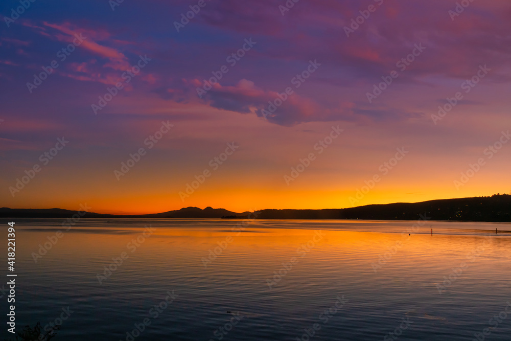 Mount Ngauruhoe and Ruapehu volcanic mountains in the distance as sunset turns to night viewed from Lake Taupo