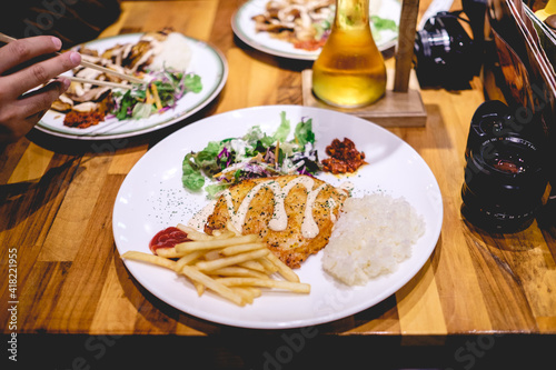 Fried chicken, french fries, rice and salad in a white plate and a camera lens in a wood table, Japan
