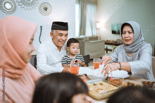 breaking the fast. muslim asian with hijab having iftar dinner together at home sitting on dining table photo