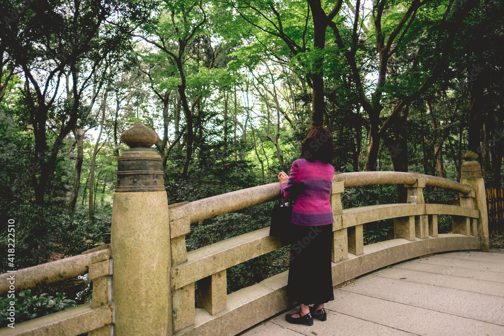 Fototapeta premium Old woman at stone bridge in the forest in the Meiji Shrine at Yoyogi Park, Tokyo, Japan