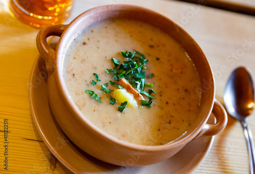 Close up of polish dish, zurek cream soup served with greens in bowl on table