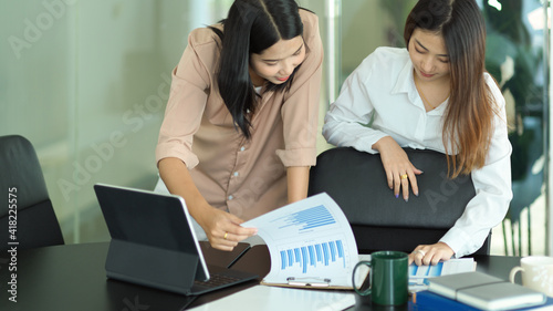 Two female office worker consulting on their project with paperwork in meeting room