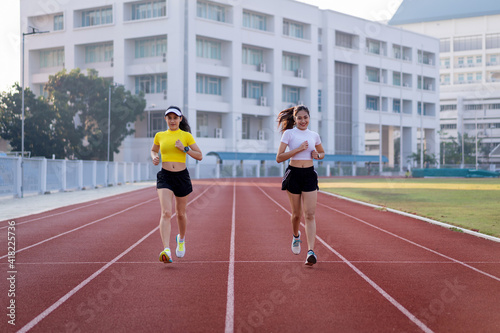 Two young Asian women in sports outfits jogging on running track in city stadium in the sunny morning to keep fitness and healthy lifestyle. Young fitness women run on the stadium track © EduLife Photos