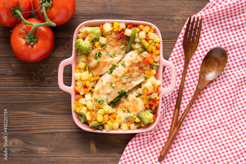 Homemade baked chicken with different seasonings and vegetables on a dark wooden background.