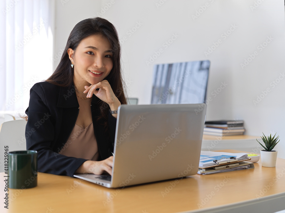 Female entrepreneur smiling to camera while working with laptop in office room Female entrepreneur smiling to camera while working with laptop in office room