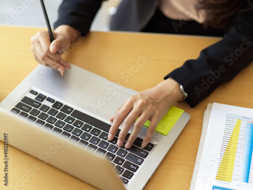 Businesswoman hand typing on laptop keyboard on wooden table in office room