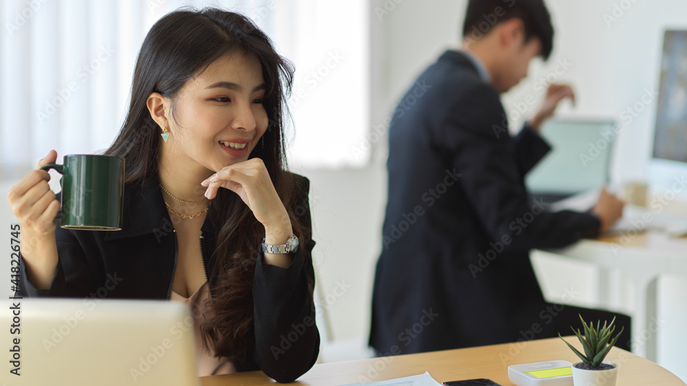 Businesswoman smiling and holding coffee cup while relaxing at workplace Businesswoman smiling and holding coffee cup while relaxing at workplace