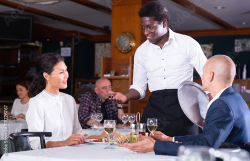 Friendly african american waiter talking with restaurant guests  recommending dishes for lunch