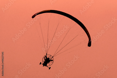 Silhouette of the Paramotor gliding and flying In the air through soft sunlight sky