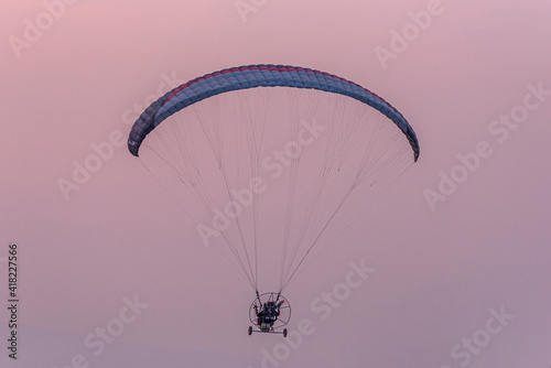 Silhouette of the Paramotor gliding and flying In the air through soft sunlight sky