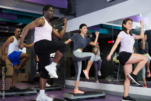 Concentrated athletic young adult people working out with aerobic steppers in gym
