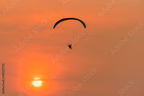 Silhouette of the Paramotor Gliding And Flying In The Air through soft sunlight sunset sky.