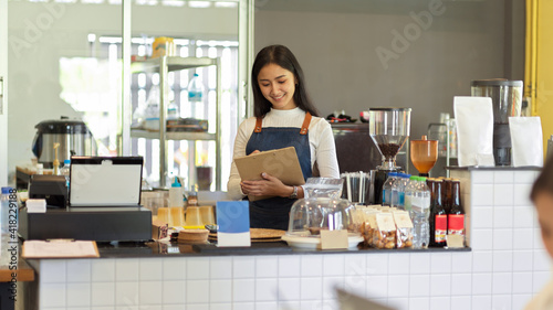 Female barista with apron writing an order while standing at counter bar in coffee shop