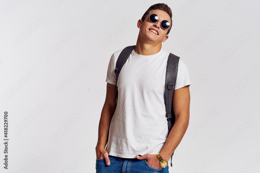man in sunglasses with a backpack on his back and in a white t-shirt on a light background cropped view of emotion man in sunglasses with a backpack on his back and in a white t-shirt on a light background cropped view of emotion