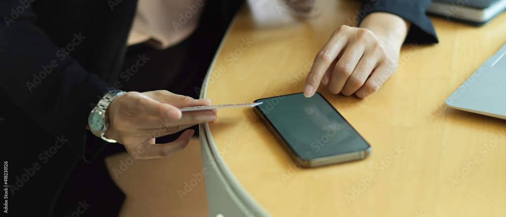 Naklejka premium Businesswoman online paying on smartphone while sitting at workplace