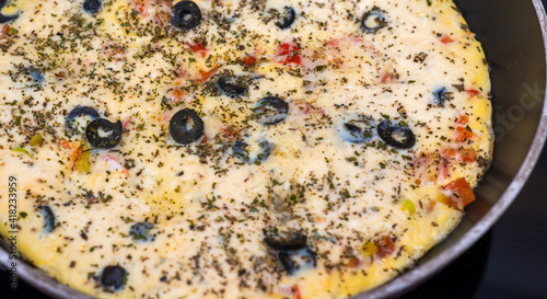 Cooked omelette in a round frying pan, top view. Eggs, milk, cheese, olives, tomatoes, spices.