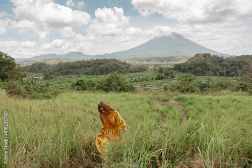 Happy young travel  girl in yellow dress walking in rice field in Bali with view on famous volcano Agung. Trevelling to clean places of Earth and discovering beauty of nature photo