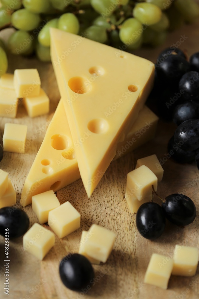 maasdamer cheese. Piece of cheese maasdam or maasdamer,green and black grapes brush on wooden board on brown background.Hard cheeses. Dairy products.Healthy and tasty .Switzerland maasdam cheese maasdamer cheese. Piece of cheese maasdam or maasdamer,green and black grapes brush on wooden board on brown background.Hard cheeses. Dairy products.Healthy and tasty .Switzerland maasdam cheese