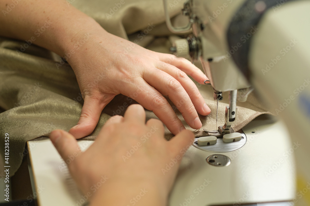 Female hands stitching white fabric on professional manufacturing machine at workplace. Close up view of sewing process. Light blurred background