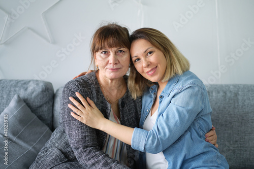 Head shot of beautiful adult daughter hug older mother at home, happy female two age generation family love