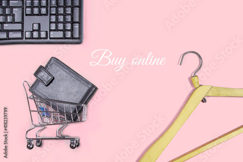 Flat lay collage of keyboard, wooden hangers, cardholder in shopping cart isolated on pink background. Buy online on internet concept. Feminine blog design
