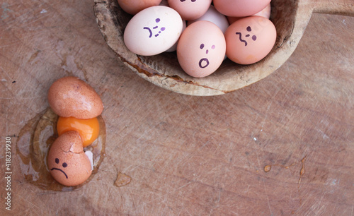 Human faces are drawn on the eggs and a funny concept photo has been prepared. Broken egg and egg yolk, egg whites on wooden background. Copy space for your text.