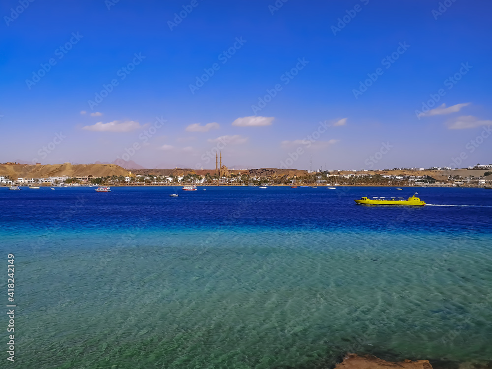 Panorama of Sharm El-Maya Bay with a yellow tourist boat in the turquoise-azure water of the Red Sea in Sharm El Sheikh (Egypt). Tropical landscape of tourist asian-african city