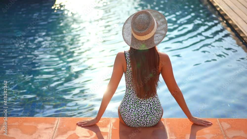 A woman sitting on the edge of a resort pool with her back to the ...