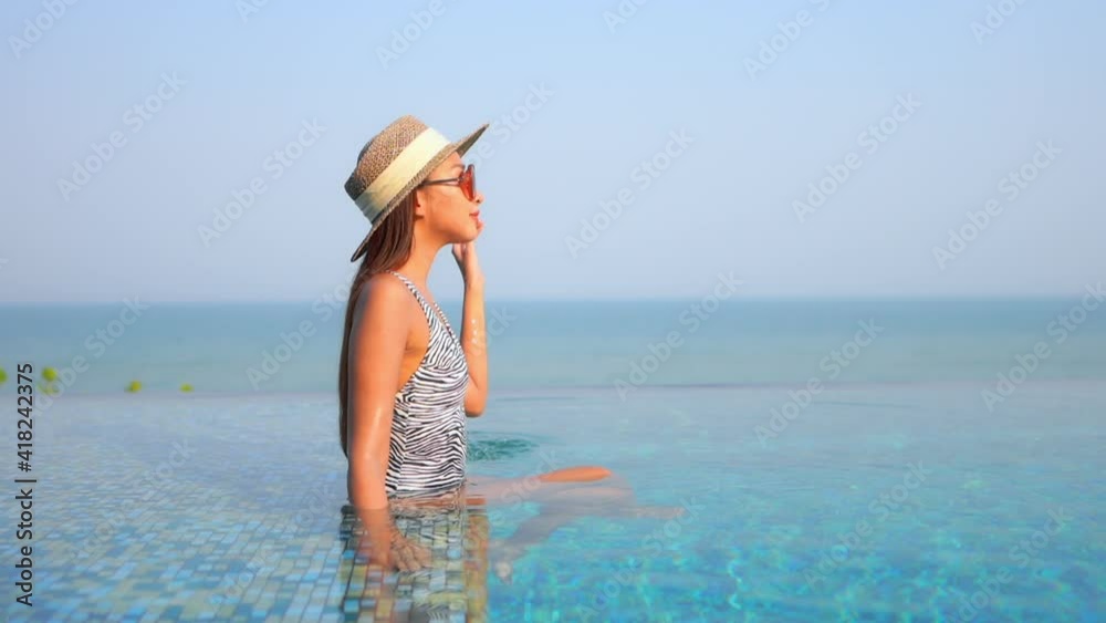 Classy young asian sitting in shallow water of infinity swimming pool on sunny day, exotic caribbean vacation concept, full frame Classy young asian sitting in shallow water of infinity swimming pool on sunny day, exotic caribbean vacation concept, full frame