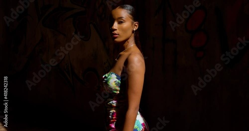 A young girl turns while standing in a ray of sunlight with grafitti on the wall in the bckground photo