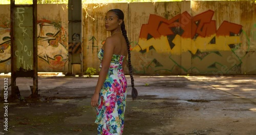 Sexy Caribbean girl in a long flowing dress walks toward grafitti on the wall before turning around photo