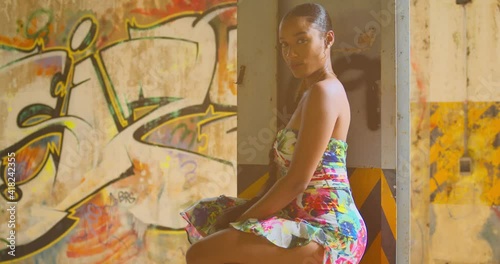 Caribbean girl squats in her flower dress with grafitti on the wall in the background photo