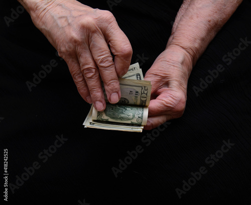 In the old woman's hands are the dollars she counts. Black background. Concept - need help