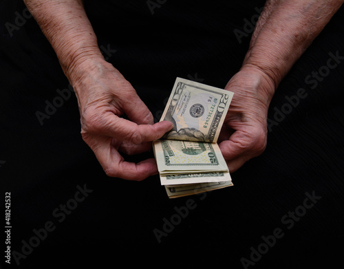 In the old woman's hands are the dollars she counts. Black background. Concept - need help