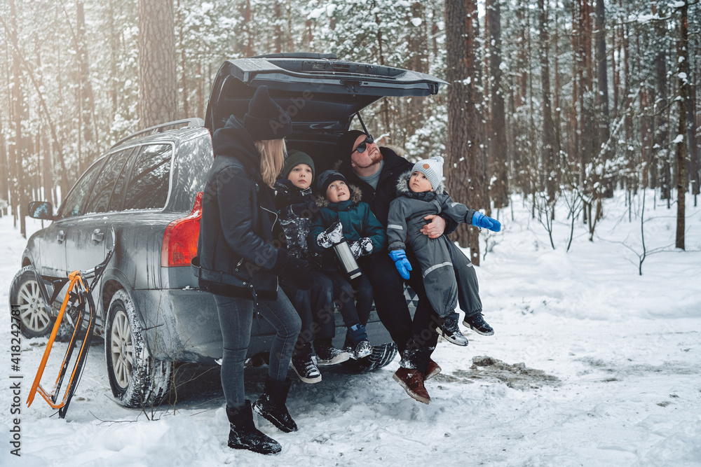 Winter portrait of a carefree boys they sit on car trunk with their father and mother and enjoy their vacation in forest.