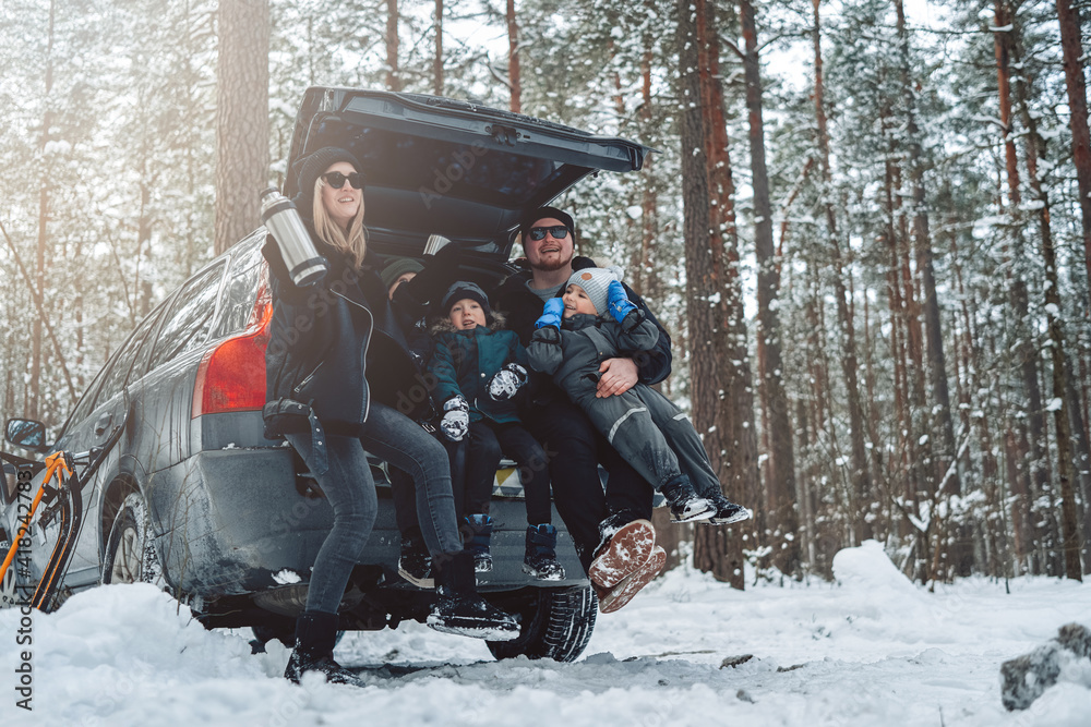 Vacations and enjoynment of a caucasian family. Three boys with their parents sit on car trunk in winter forest in daytime.