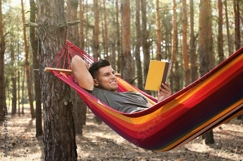 Man with book relaxing in hammock outdoors on summer day