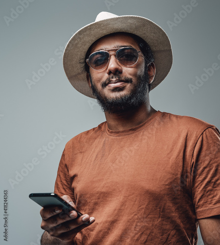 Self confident and bearded indian guy in orange shirt poses in gray background holding his smartphone. photo