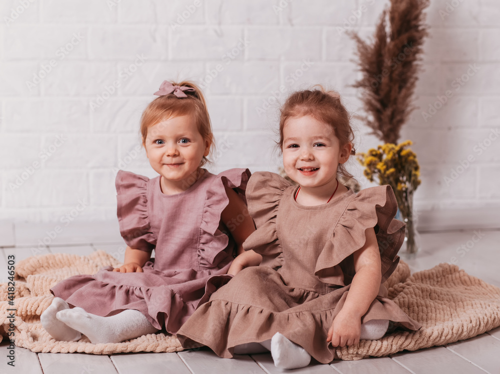 Two pretty little girls sit and smile in a room on the floor Two pretty little girls sit and smile in a room on the floor